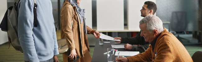 Profissionais realizando atendimento e conferência de documentos em ambiente corporativo, representando processos administrativos e gestão de pessoas.