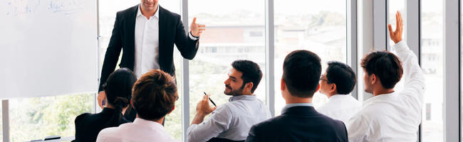 Colaboradores participando de uma apresentação em ambiente corporativo, com profissional conduzindo a conversa diante da equipe.
